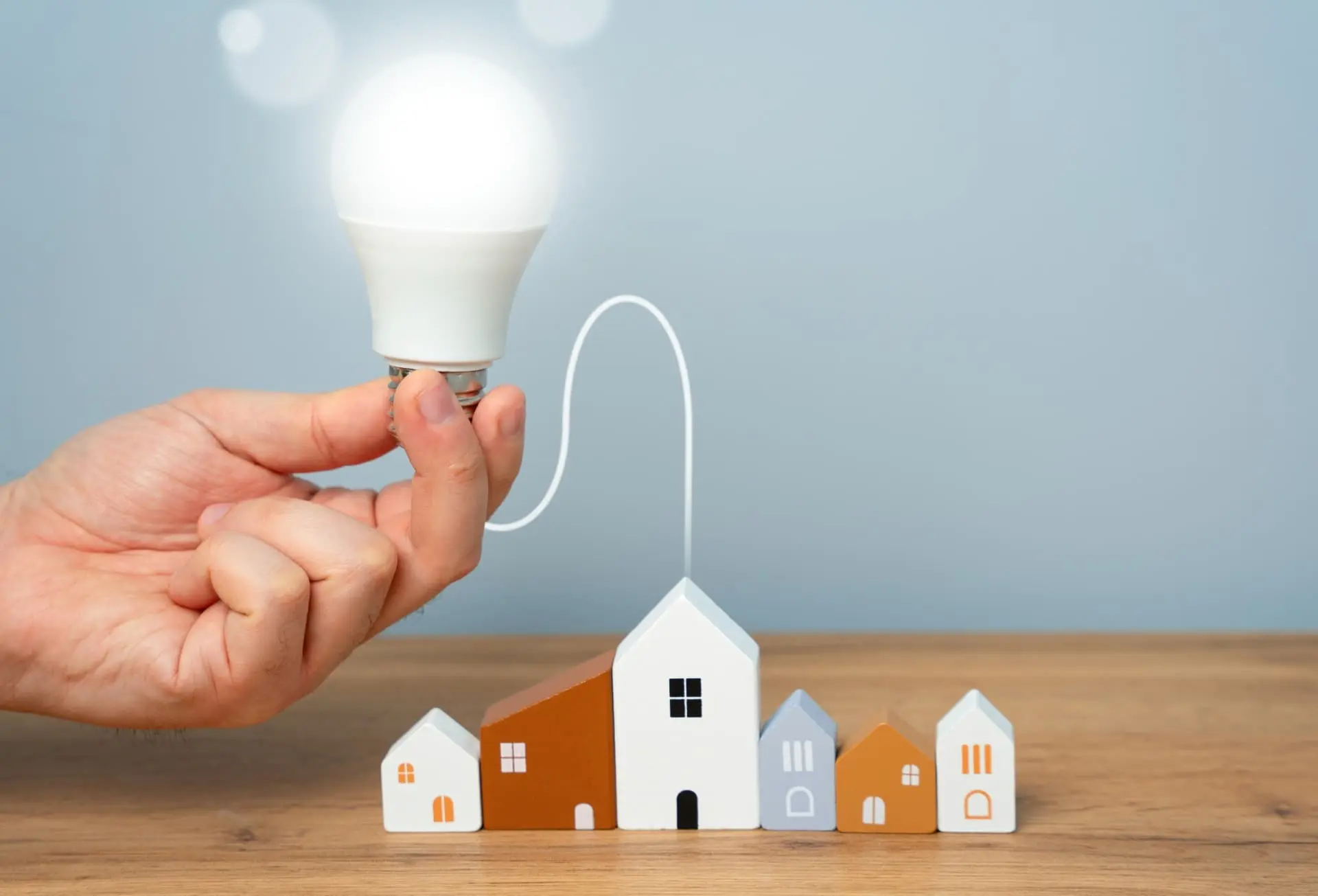 mão segurando uma lâmpada conectada a uma maquete de casas